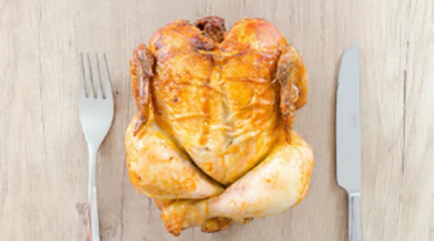 Whole roasted chicken on a wooden table with fork and knife placed beside it.