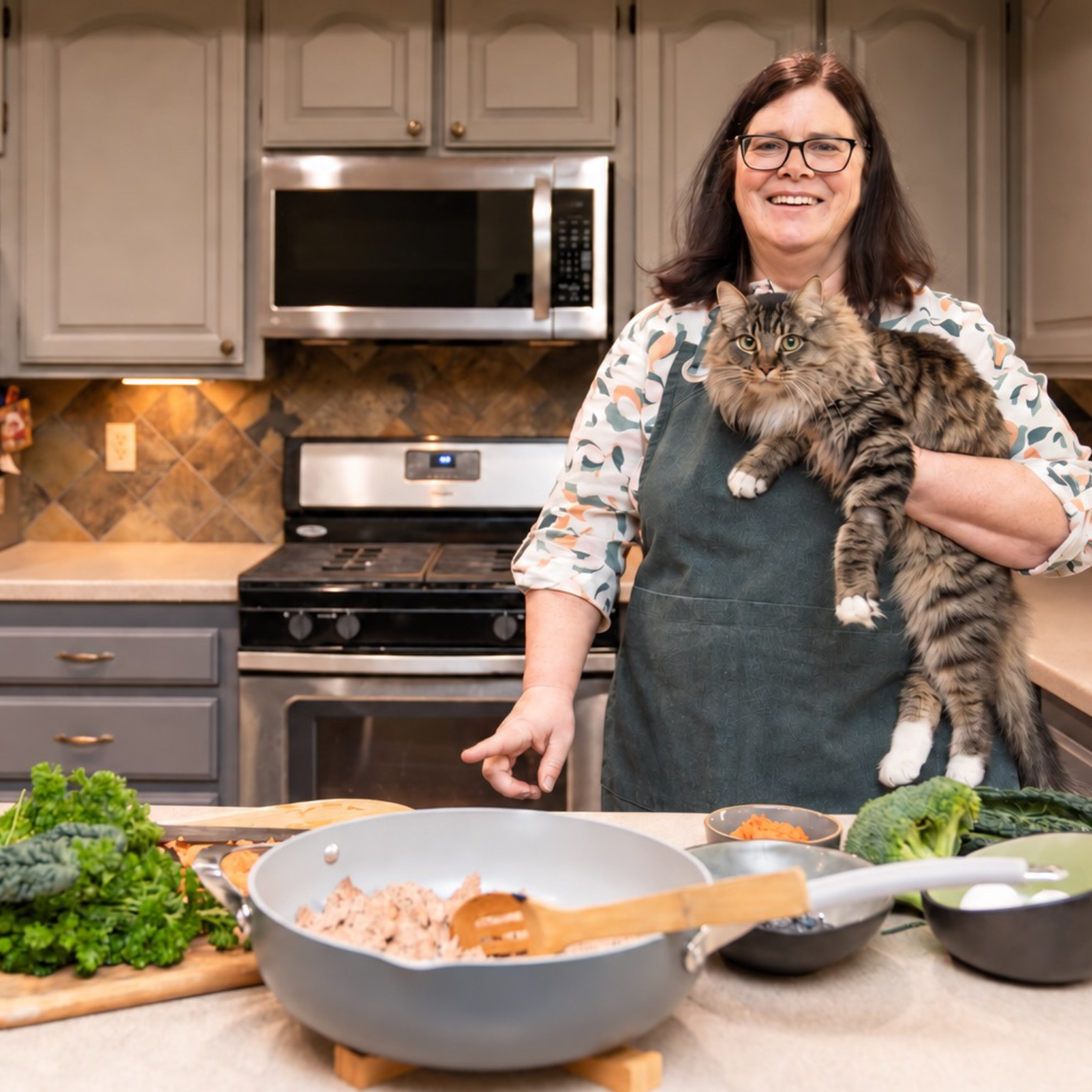 Dr. Dody holding a long-haired tabby cat in her kitchen while preparing homemade cat food